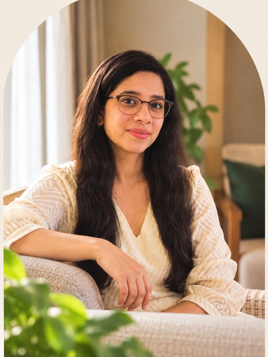 Anjana Iyer in glasses and a linen top, seated in an armchair at home.